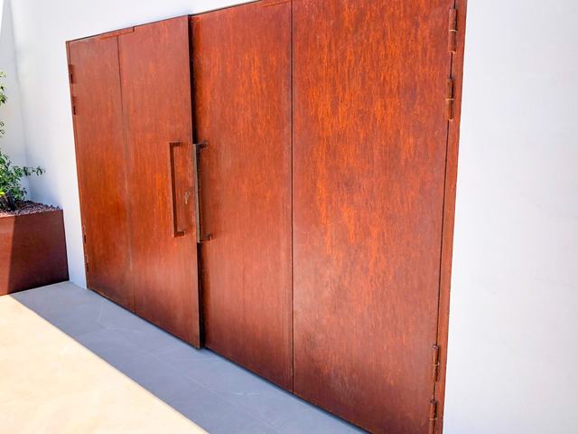 Puerta de libro de acero corten en una fachada blanca