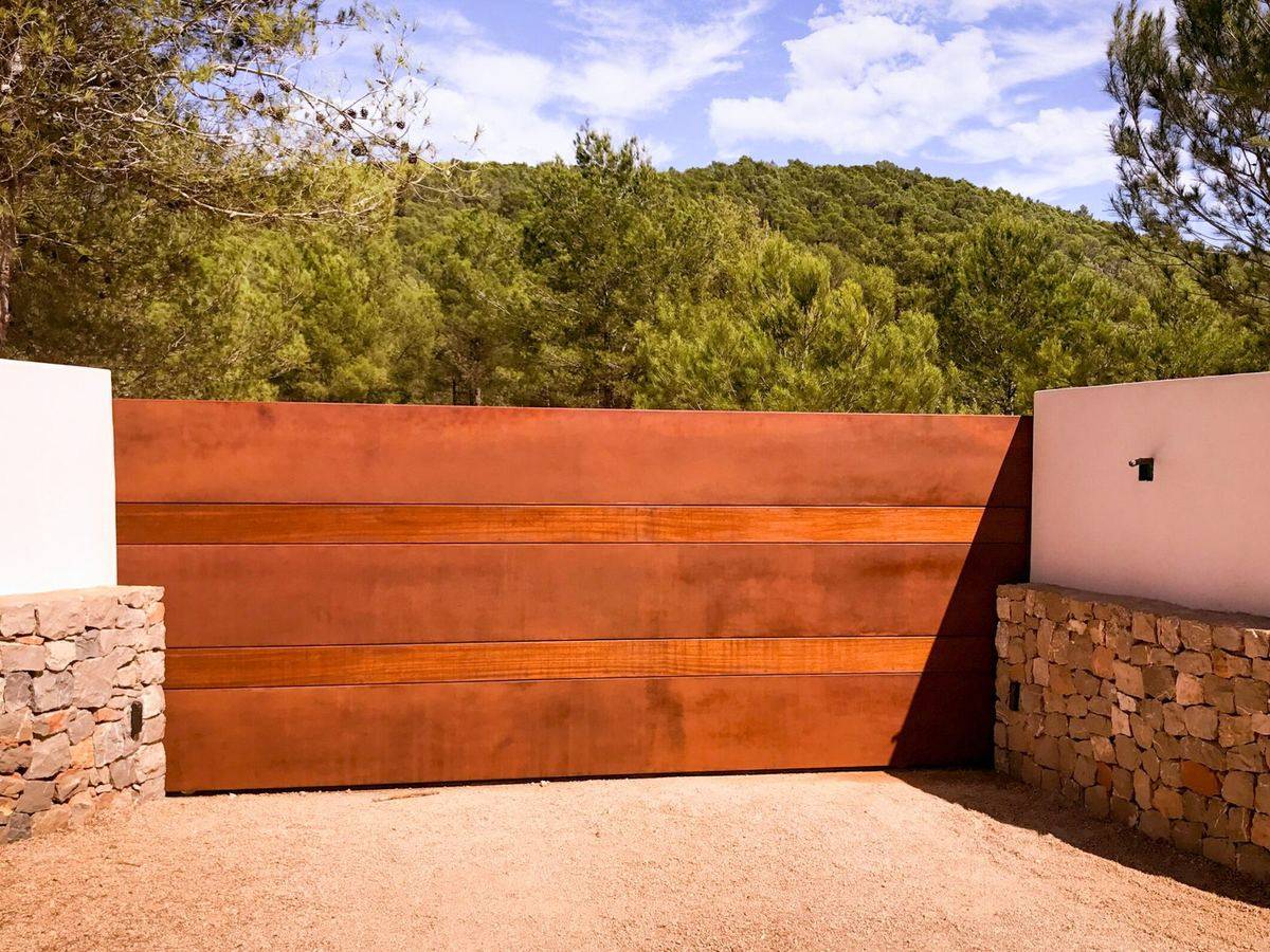 Vallado de acero corten y madera entre muros de piedra