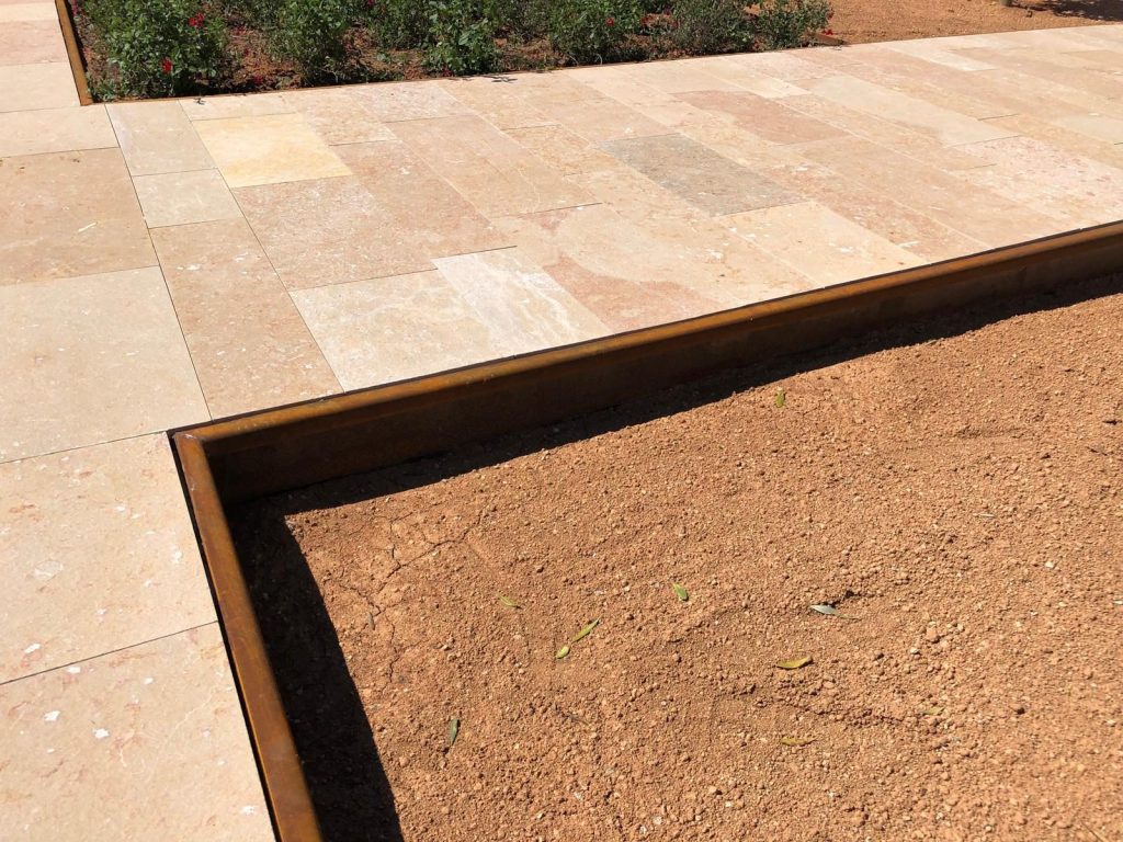 Bordillo de acero corten que separa un camino de piedra y un jardín