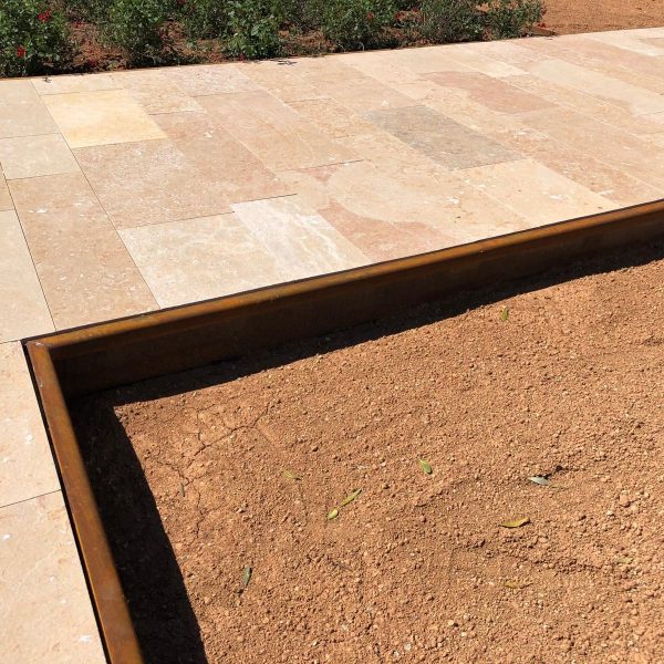 Bordillo de acero corten que separa un camino de piedra y un jardín
