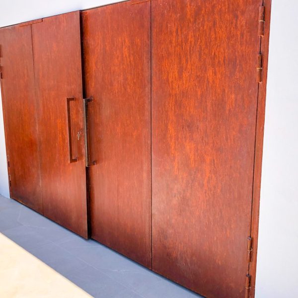 Puerta de libro de acero corten en una fachada blanca