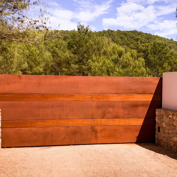 Vallado de acero corten entre muros de piedra a la entrada de una vivienda